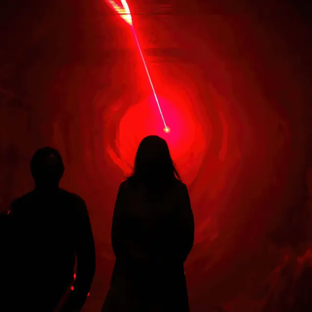 FÔ-LE-GO: duas pessoas em silhueta diante de um feixe de laser vermelho