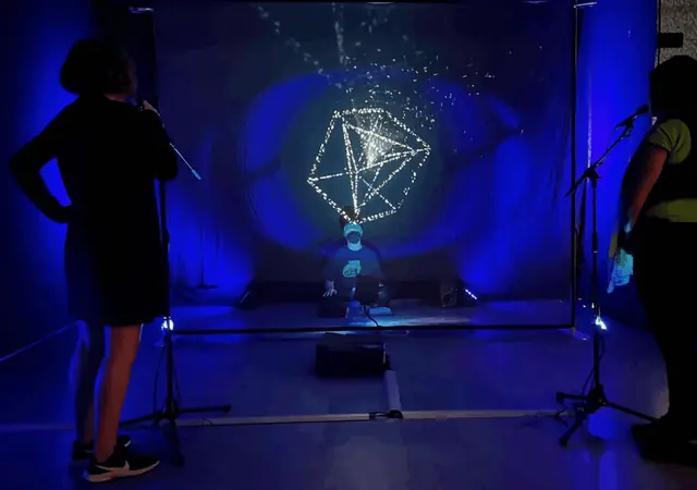 KIMA Resonance: holograma geométrico azul gerado pela voz, com o público à volta